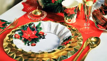 Piatti dorati e decorati con motivi floreali natalizi sopra una tovaglia addobbata per Natale