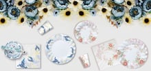 Piatti e bicchieri decorati con fiori su una tovaglia floreale, con un design elegante e colorato, perfetti per una festa a tema floreale.
