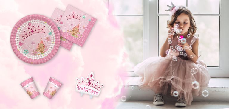 Set di articoli da festa a tema principessa, inclusi piatti, bicchieri e tovaglioli rosa con una corona e castello, accompagnato da un'immagine di una bambina che soffia bolle di sapone, indossando una corona.