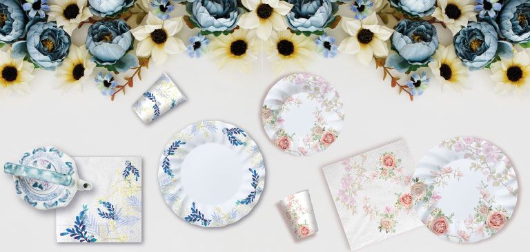 Piatti e bicchieri decorati con fiori su una tovaglia floreale, con un design elegante e colorato, perfetti per una festa a tema floreale.